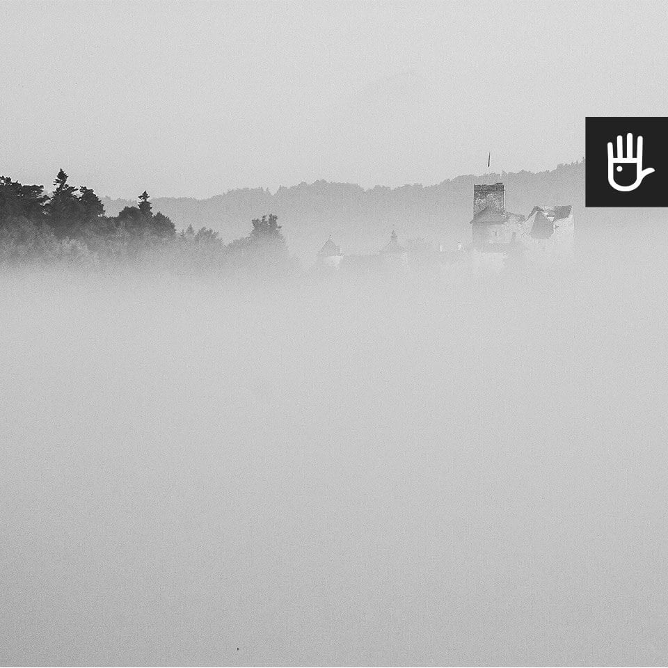 kadr czarno-białej fototapety zamek w chmurach z zamkiem i lasem we mgle
