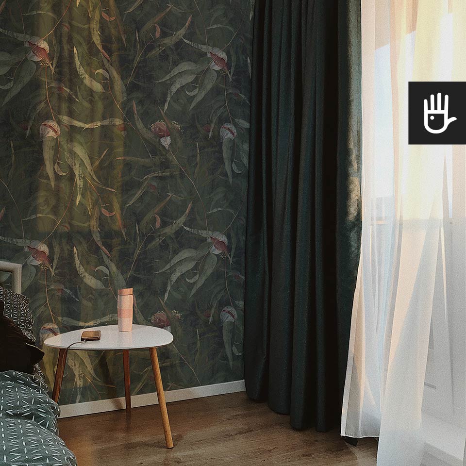 Przytulny kąt w nastrojowej sypialni z zielonymi zasłonami i piękną ścianą , na której znajduje się ścienna tapeta Kwiaty eukaliptusa z malowanymi ręcznie kwiatami i liśćmi na tle w kolorze butelkowej zieleni.