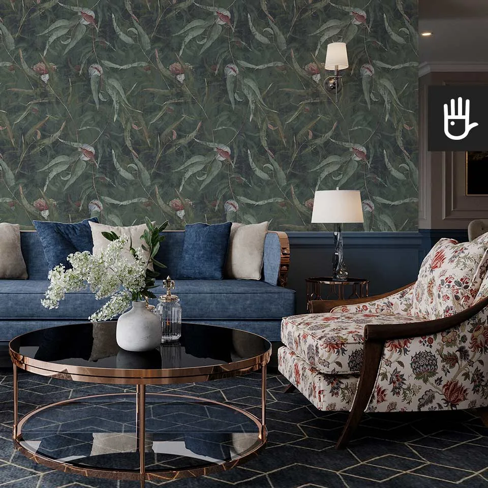 Salon w stylu Hampton z kolorową kanapą na tle ściany pokrytej zieloną tapetą ścienną z malowanymi różowymi kwiatami eukaliptusa i zielonymi listkami.