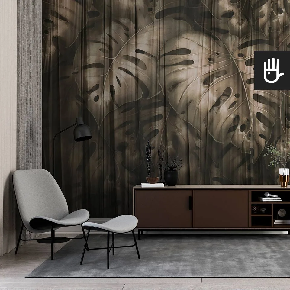 Elegancki gabinet z dekoracyjną ciemną fototapetą Złota monstera z dużymi, tropikalnymi liśćmi spowitymi przeźroczystym materiałem na ścianie za komodą.