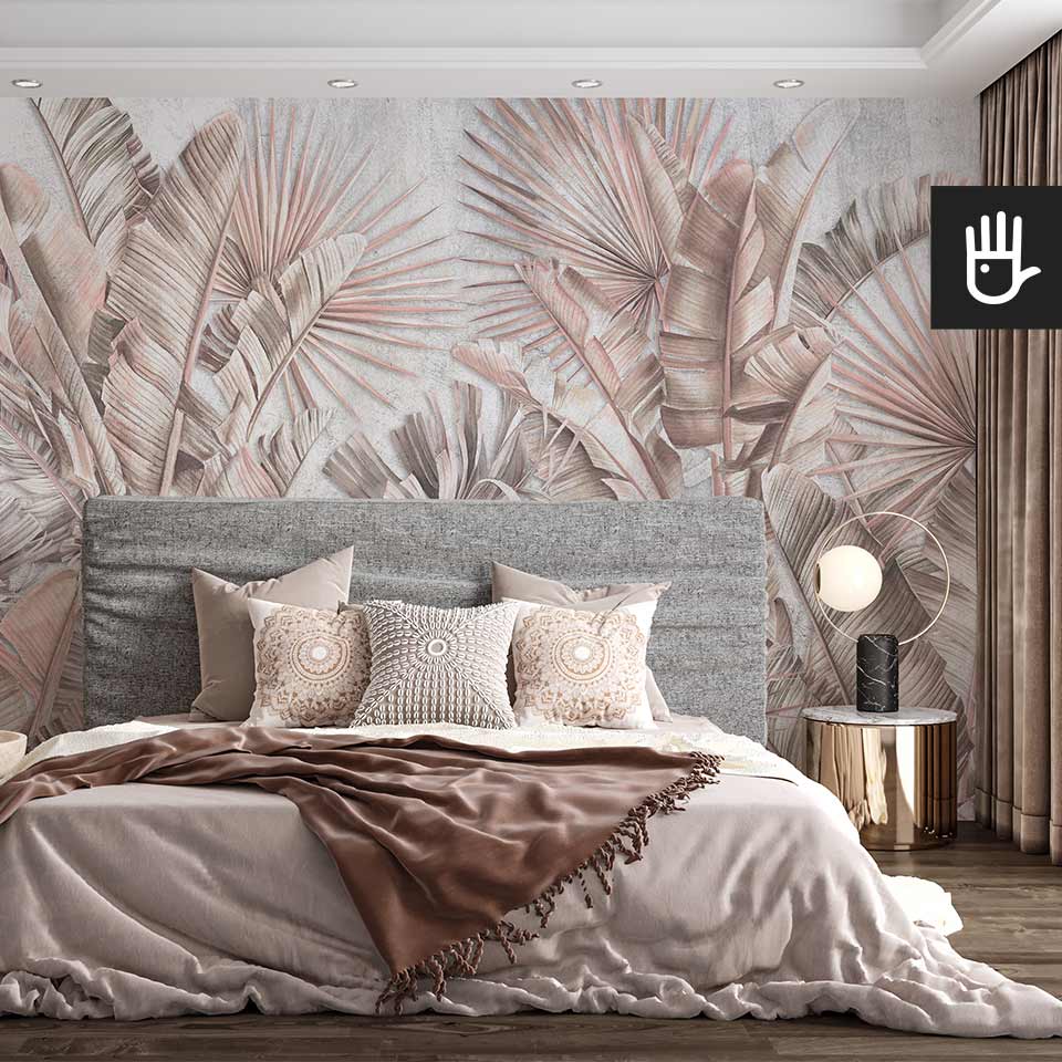 Fototapeta Pastelowa dżungla z motywem palmowych liści w kolorze pudrowego różu na ścianie za łóżkiem z tapicerowanym, szarym zagłówkiem w stylowej sypialni boho.