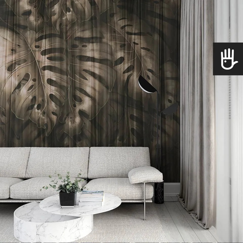 Nowoczesny salon we włoskim stylu z beżową kanapą na tle ciemnej fototapety Złota monstera z dużymi liśćmi egzotycznej rośliny w odcieniach brązu wyłaniających się zza delikatnej, prześwitującej zasłony.