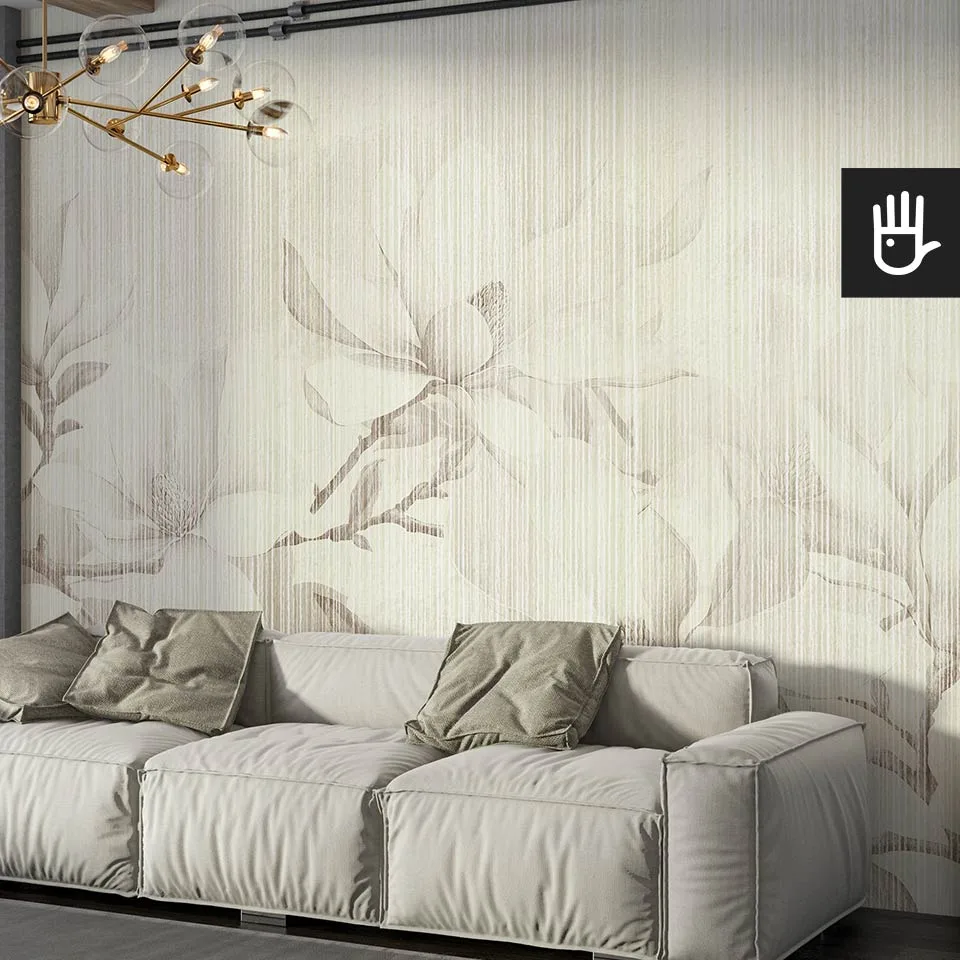 Słoneczny salon z dużą szarą kanapą z zielonymi poduszkami dekoracyjnymi i ozdobną lampą wiszącą na tle fototapety magnolie