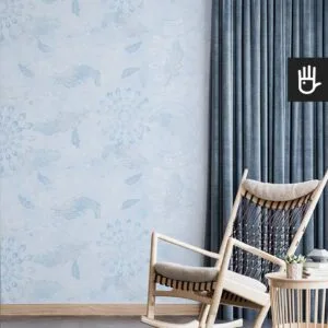Bujany fotel do czytania w stylu boho z dekoracyjnym stolikiem z książkami na tle tapety w błękitnym kolorze z delikatnym wzorem
