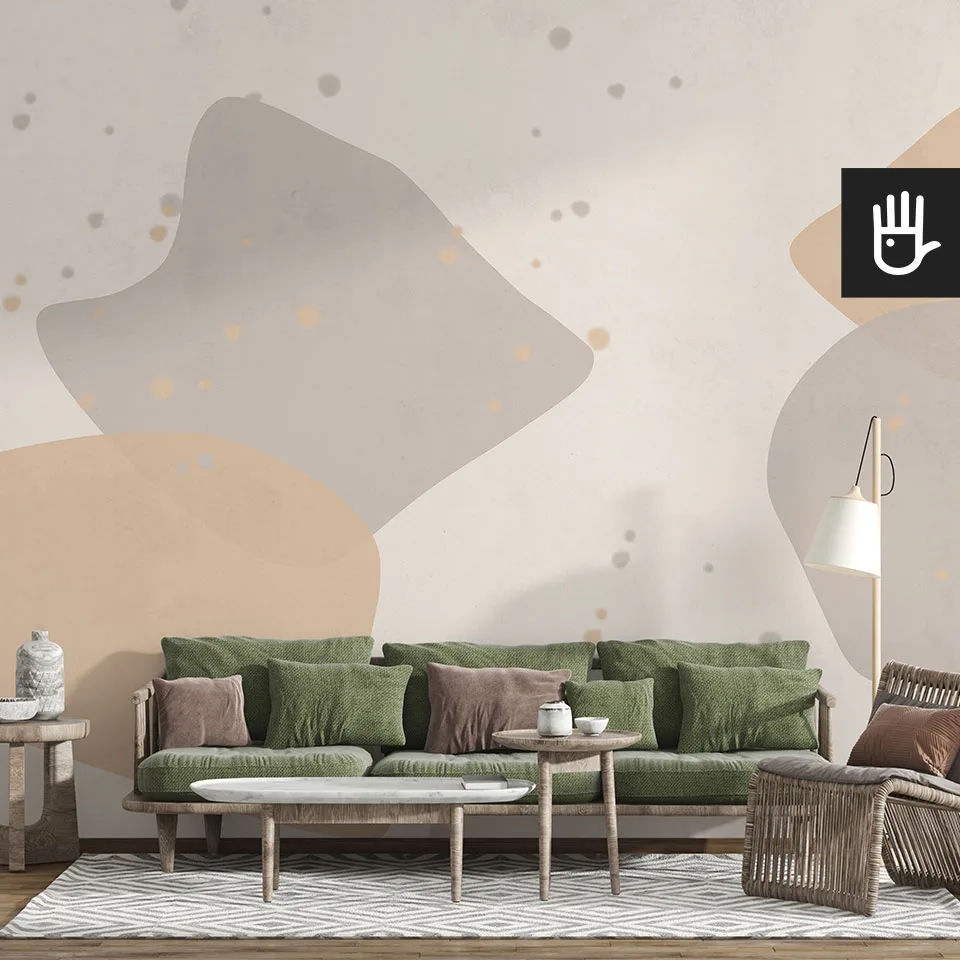 Salon w stylu boho z wiklinowym fotelem i zieloną kanapą na tle fototapety w beżowe i brązowe plamy