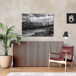 Salon w stylu retro z bordowym fotelem ze skóry i wielkim zielonym kwiatem na tle ściany ze strukturą betonu z przywieszonym obrazem przedstawiającym góry