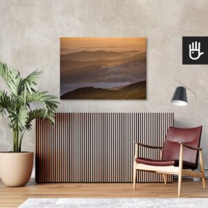 Salon w stylu retro z bordowym fotelem ze skóry i wielkim zielonym kwiatem na tle ściany ze strukturą betonu z przywieszonym obrazem przedstawiającym góry