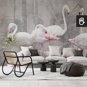 Nowoczesny salon z dużą beżową kanapą, czarnymi dekoracyjnymi stolikami kawowymi i ratanowym fotelem udekorowana abstrakcyjną fototapetą z flamingami na szary tle