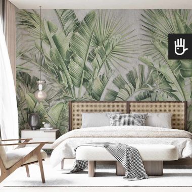Fototapeta Miejska dżungla z motywem palmowych liści w kolorze zielonym na ścianie za łóżkiem z plecionym zagłówkiem w stylowej sypialni w stylu quiet luxury.