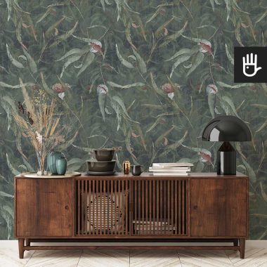 Elegancka, drewniana komoda w stylu PRL na tle zielonej ściany w stylu vintage z położoną tapetą Kwiaty eukaliptusa z malowanymi liśćmi w zielonym kolorze.